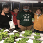 students smiling behind lettuce they grew