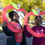 Two school age girls holding apple shaped frame outdoors.